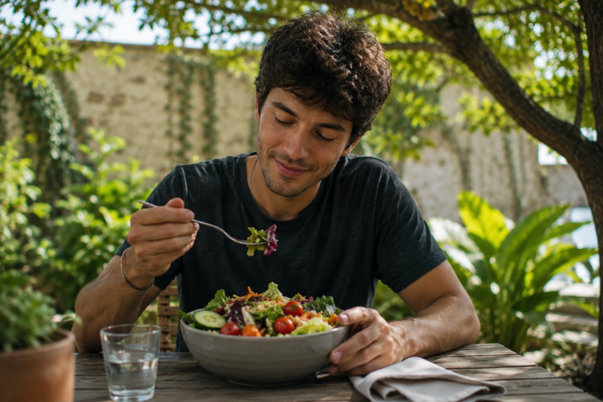 Un hombre en sus 20s disfrutando una ensalada colorida al aire libre