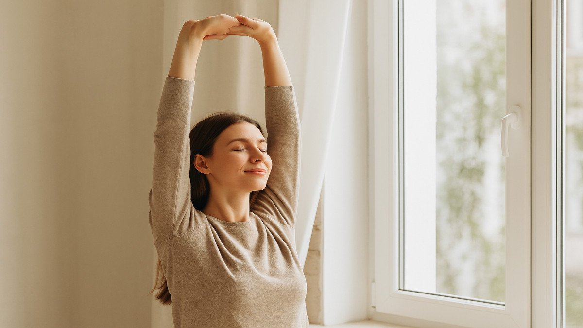 Mujer relajada estirando los brazos junto a una ventana con luz natural